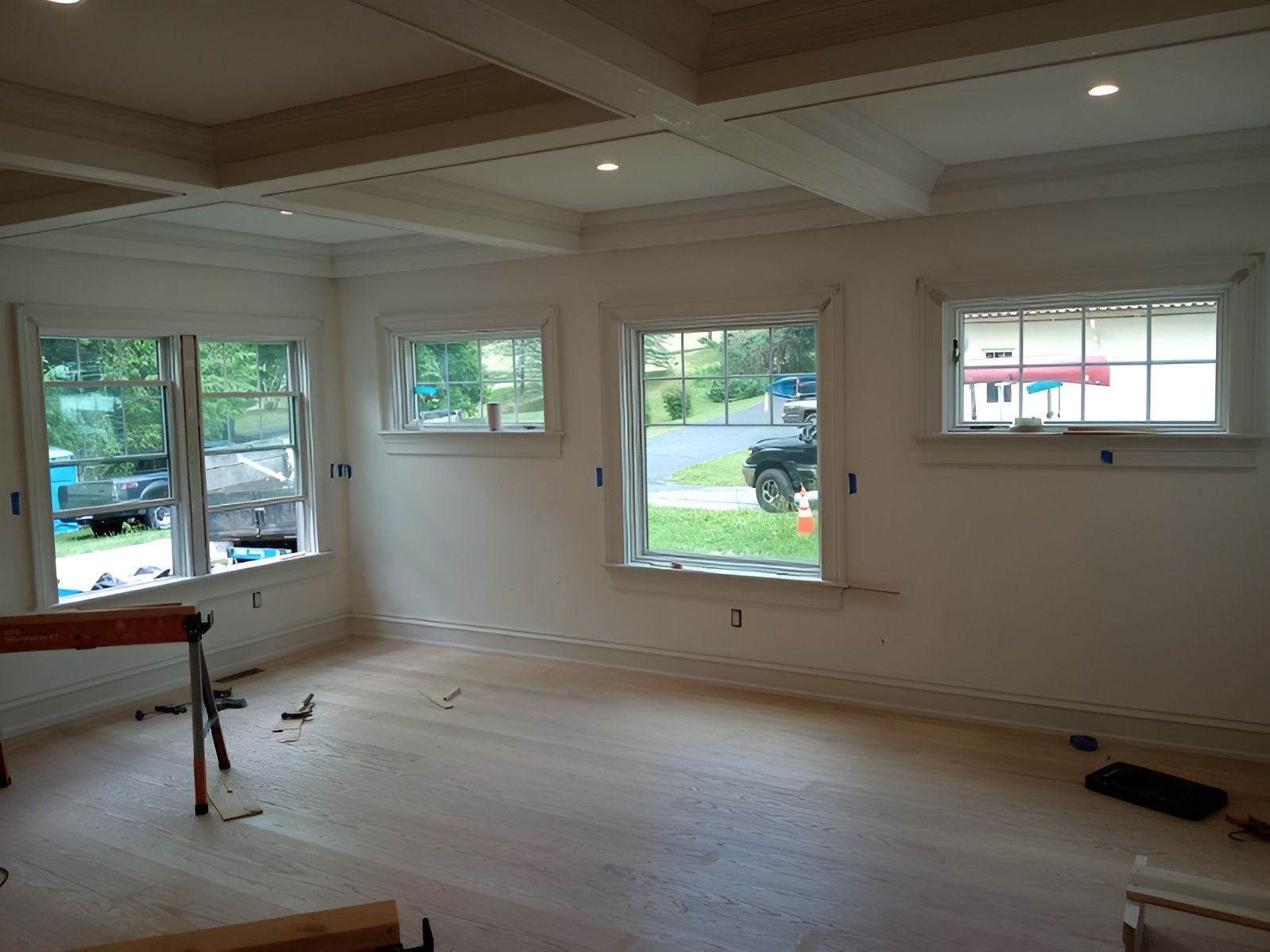 Empty room with light wood floors, white walls, windows, and a coffered ceiling.