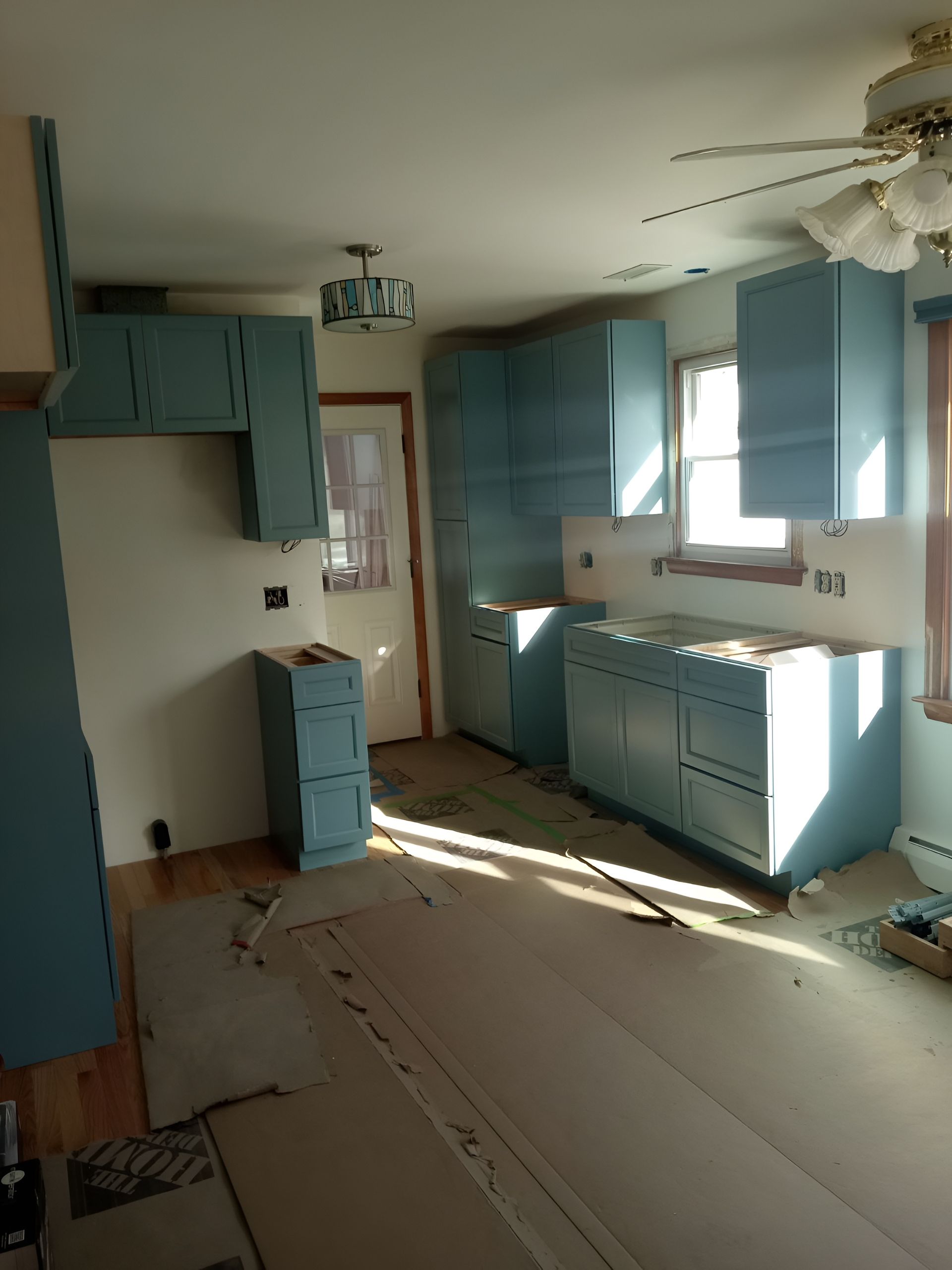 Kitchen under construction; blue cabinets against white walls, sunlight streams in.