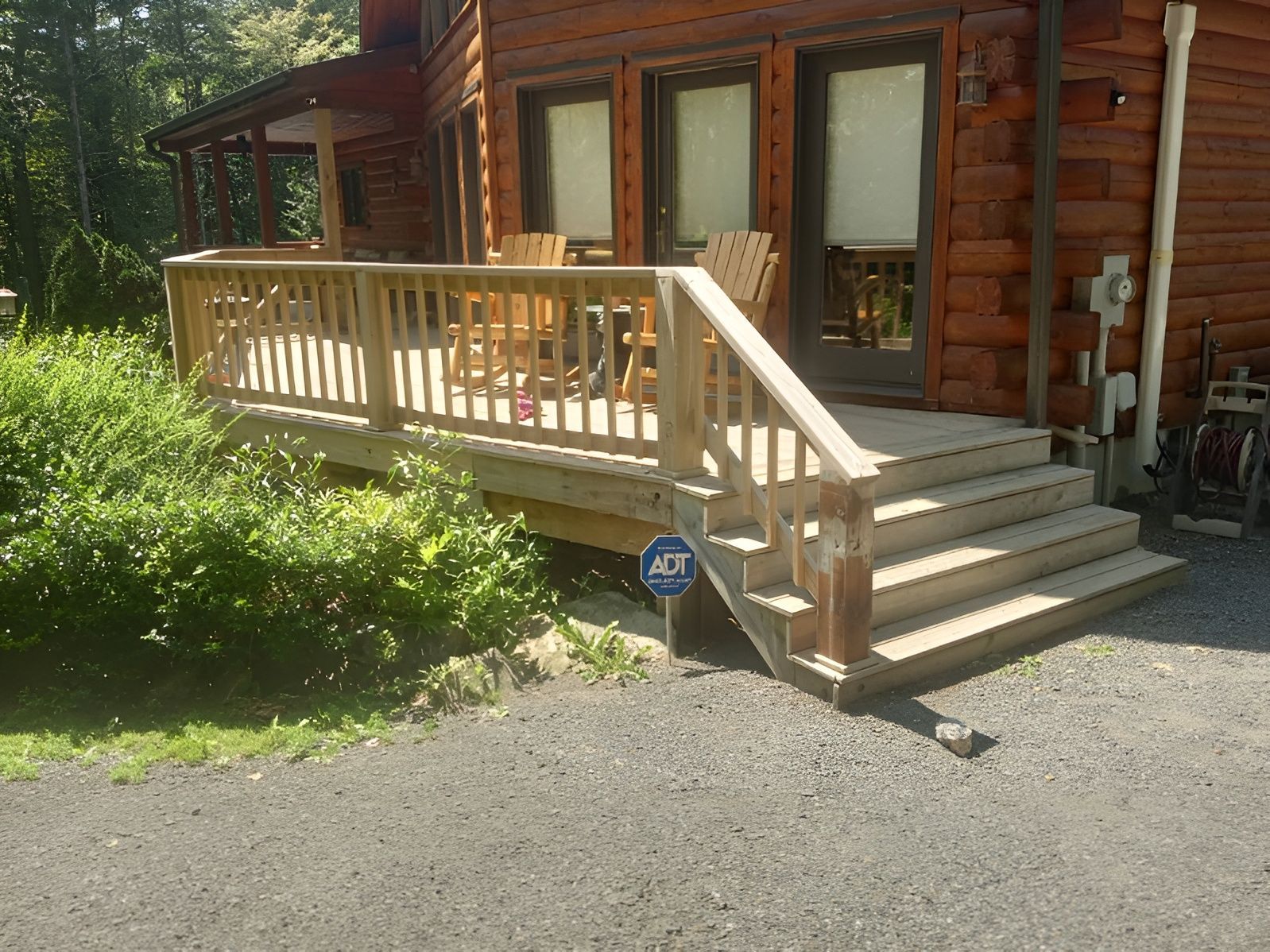 Wooden deck with stairs, railing, and chairs in front of a log cabin.