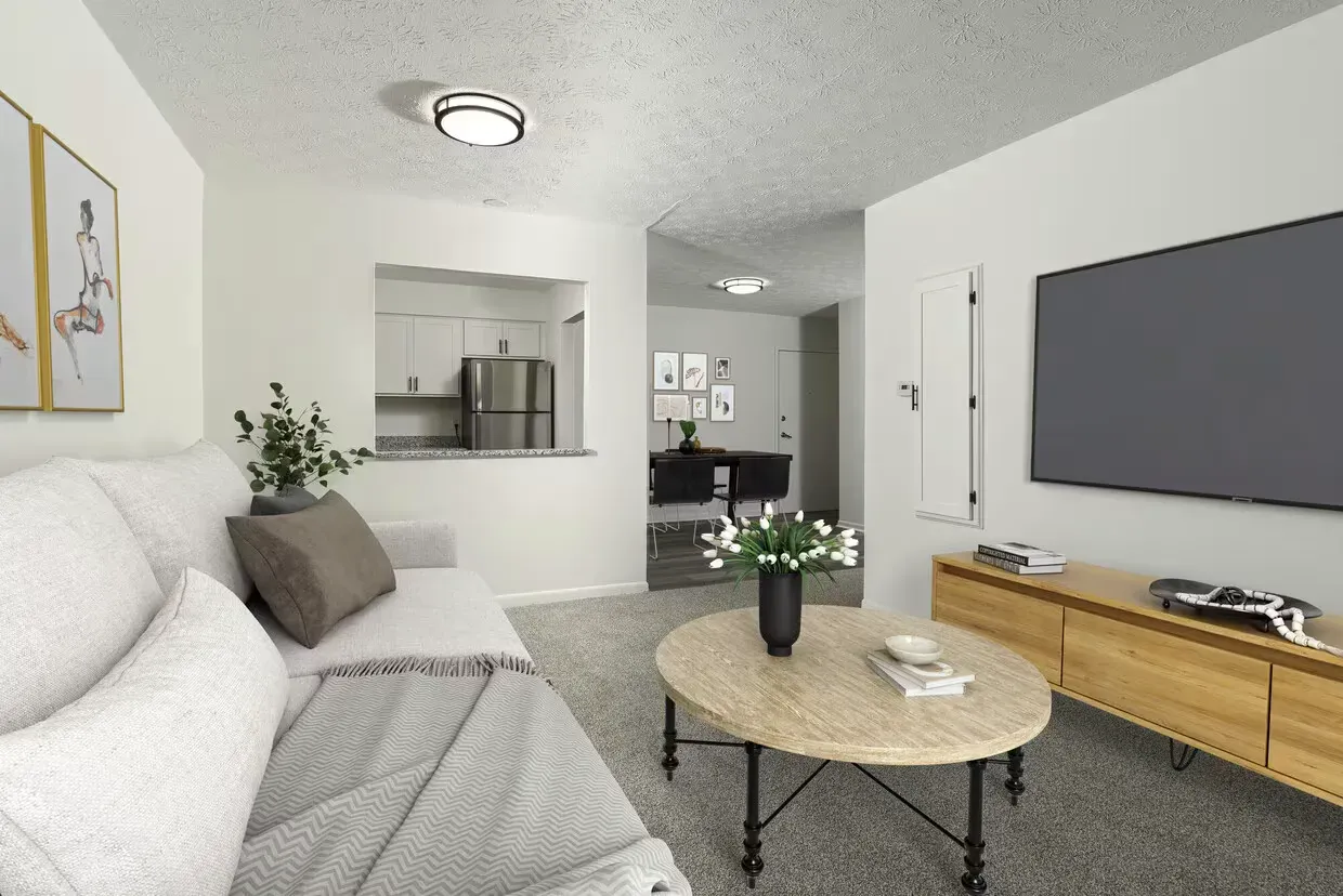 Living room with a gray sofa, round coffee table, and a wall-mounted TV; open kitchen in back at the Reserves at Arlington in Columbus, OH.
