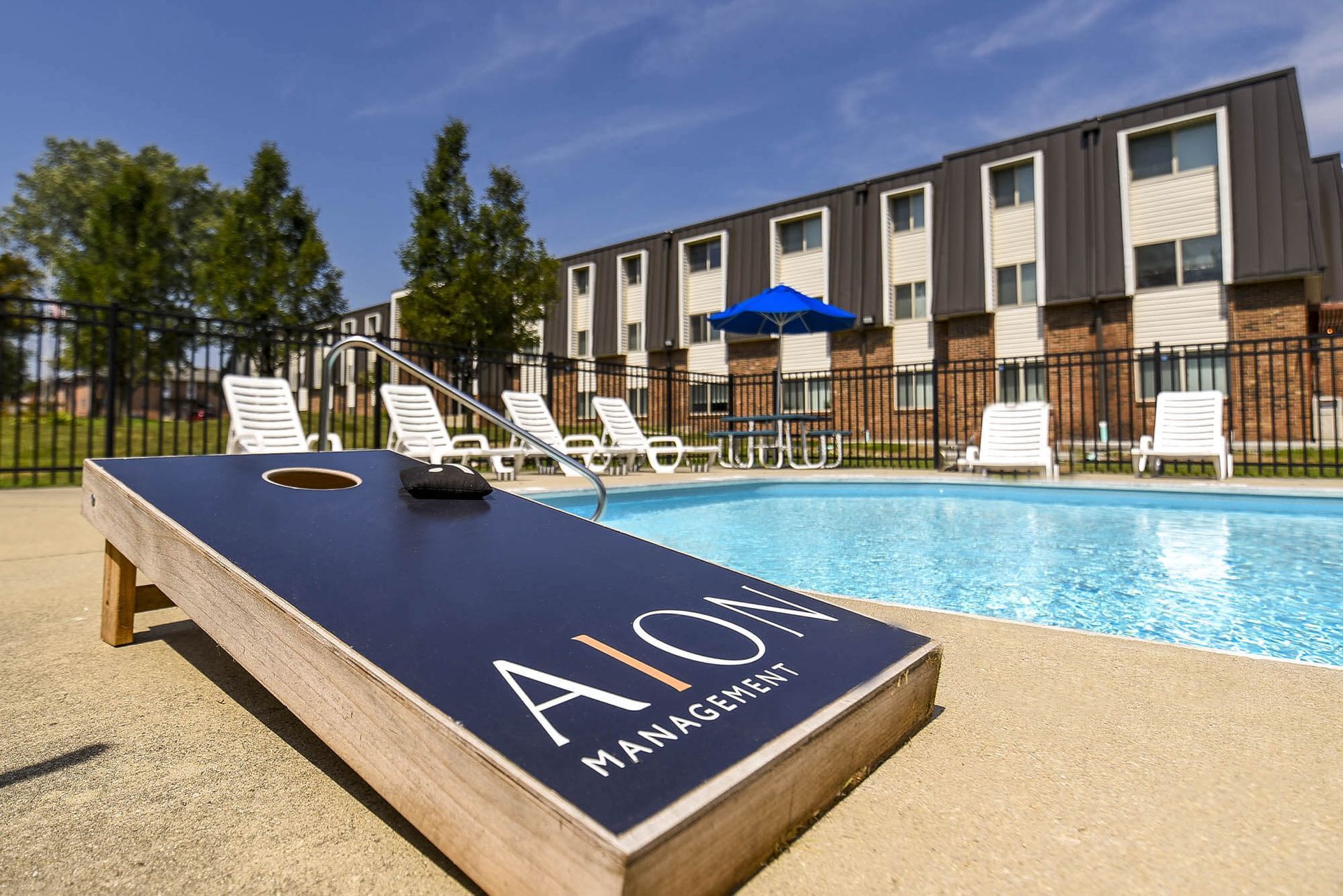Outdoor apartment poolside with lounge chairs, a blue umbrella, and a fenced yard at the Reserves at Arlington in Columbus, OH.