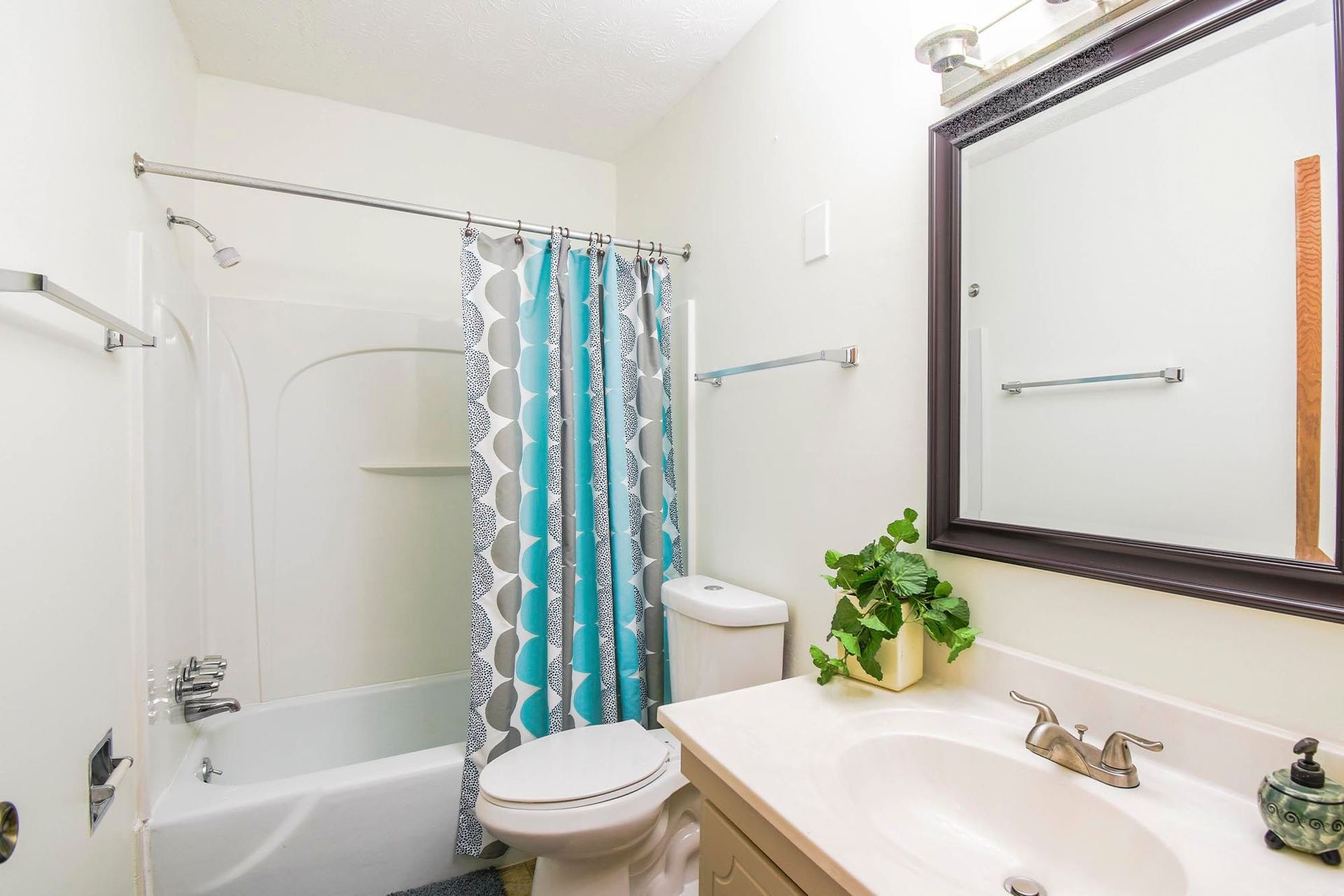 Bathroom in an apartment with a vanity, mirror, toilet, and tub/shower with teal-gray curtain at the Reserves at Arlington in Columbus, OH.