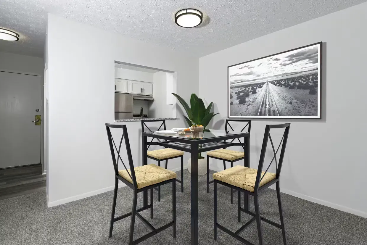 Dining area in a modern apartment with a glass table and four woven-seat chairs at the Reserves at Arlington in Columbus, OH.