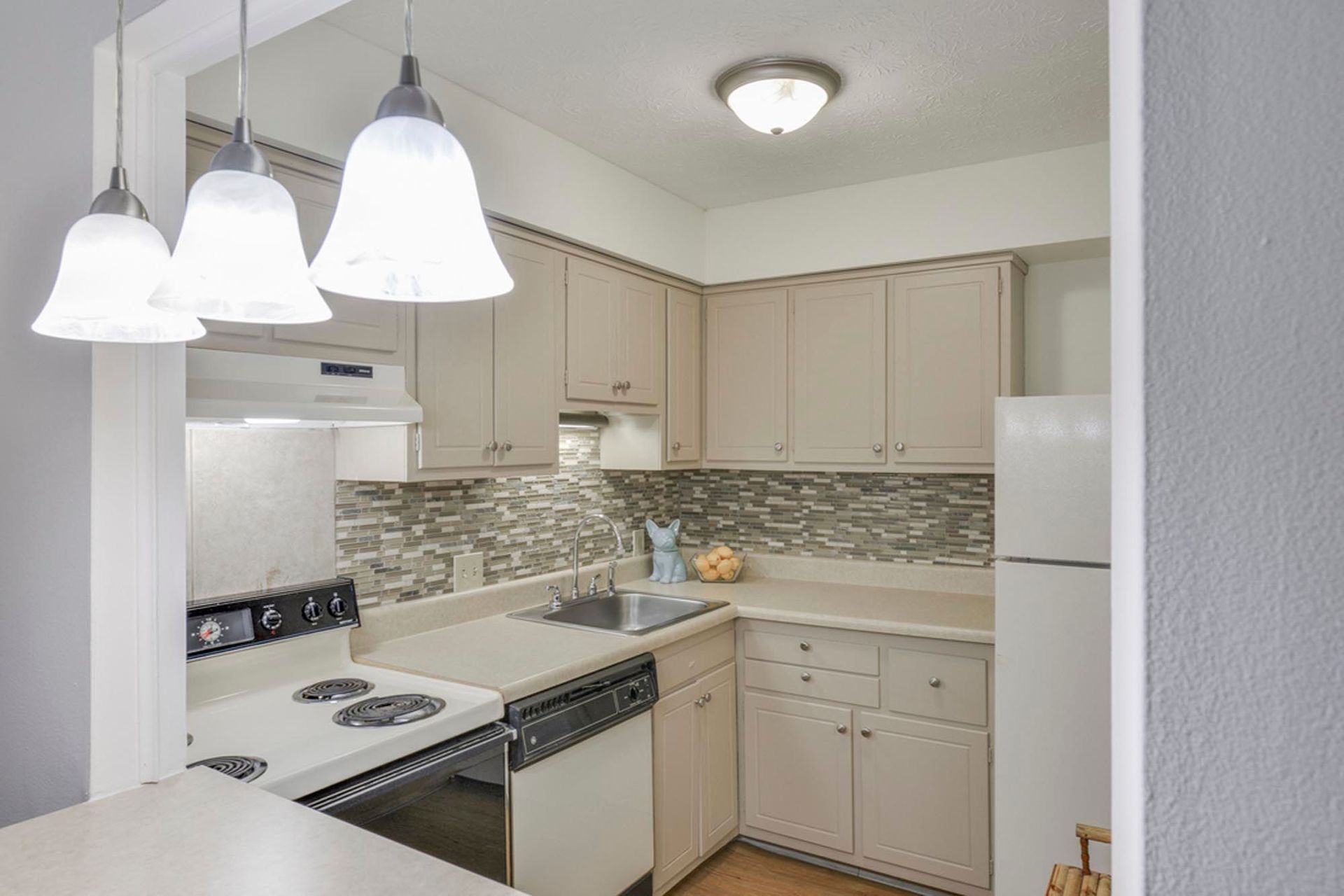 L-shaped kitchen with beige cabinets, tile backsplash, sink, stove, and dishwasher at the Reserves at Arlington in Columbus, OH.
