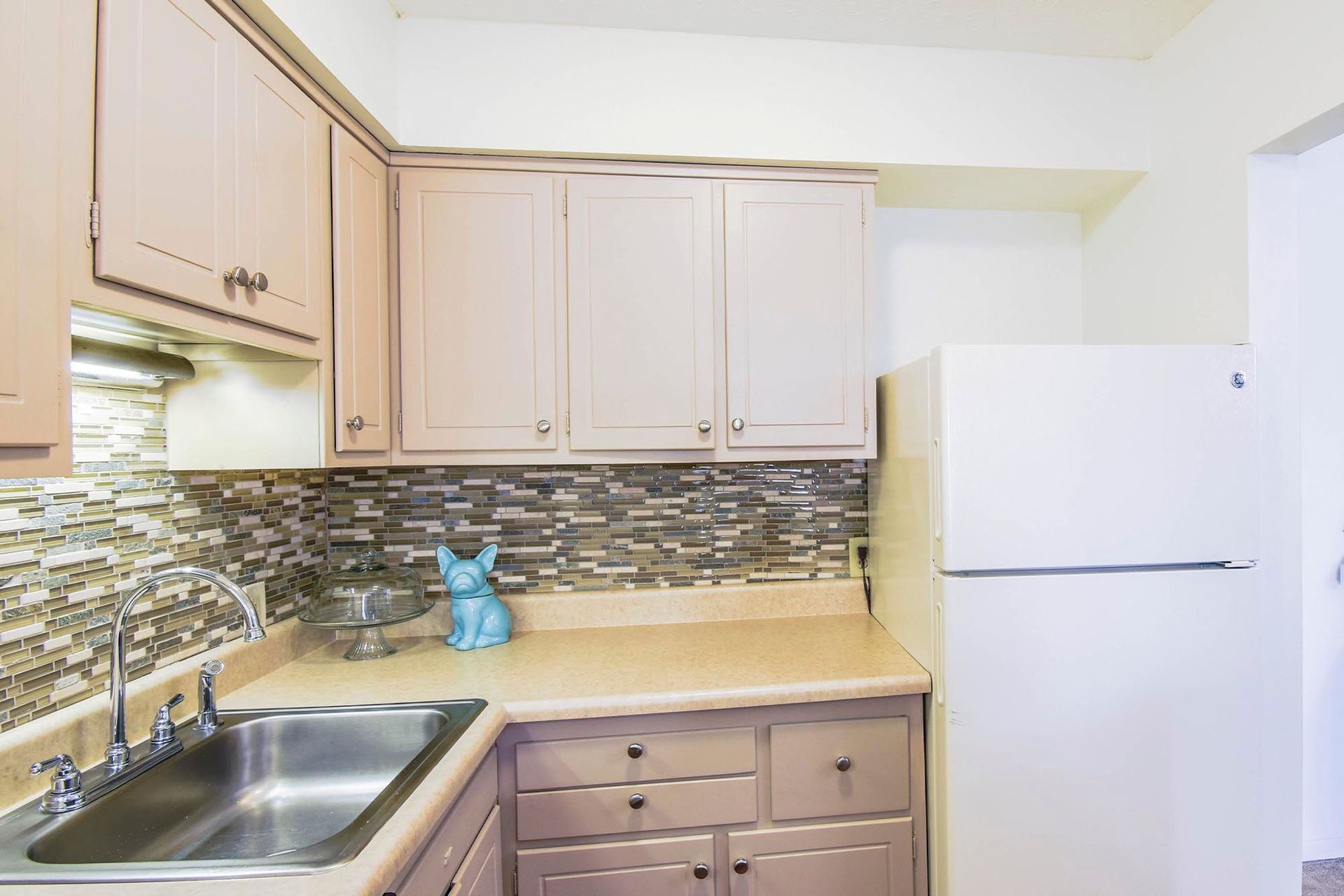 Kitchen in an apartment with beige cabinets, mosaic backsplash, sink, and a white refrigerator at the Reserves at Arlington in Columbus, OH.