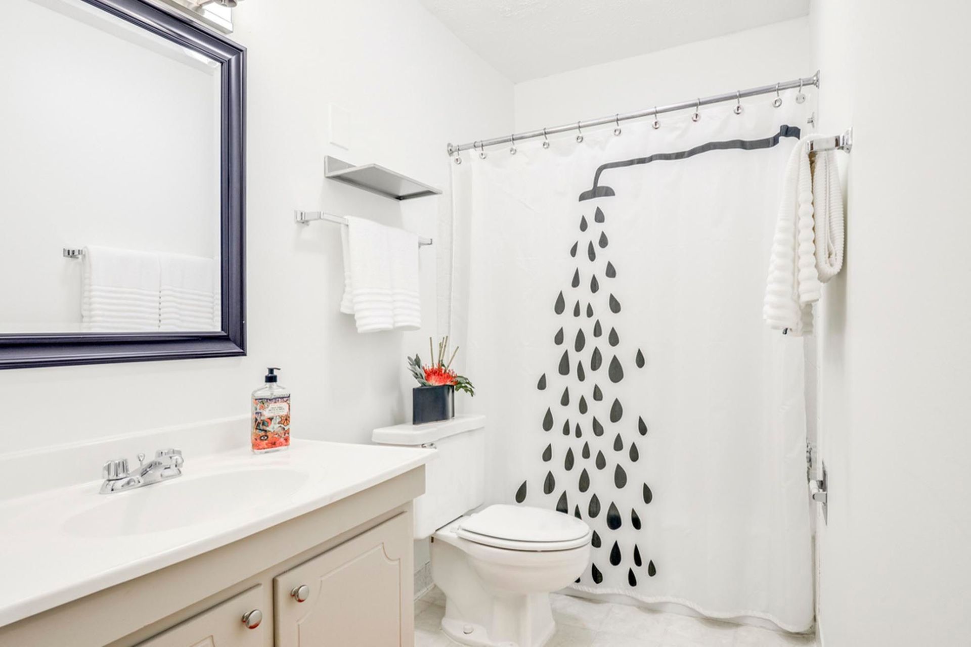 Apartment bathroom with a white vanity, sink, toilet, and shower curtain with a raindrop pattern at the Reserves at Arlington in Columbus, OH.