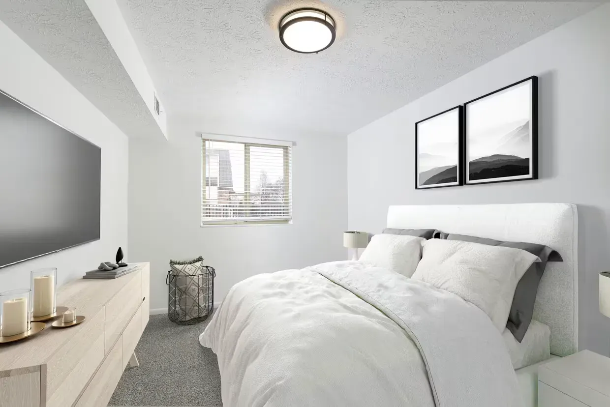 Bedroom in a modern apartment with a bed, dresser, and window at the Reserves at Arlington in Columbus, OH.