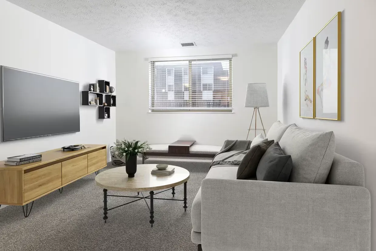 Apartment living room with gray sofa, round coffee table, TV, window, and framed art at the Reserves at Arlington in Columbus, OH.