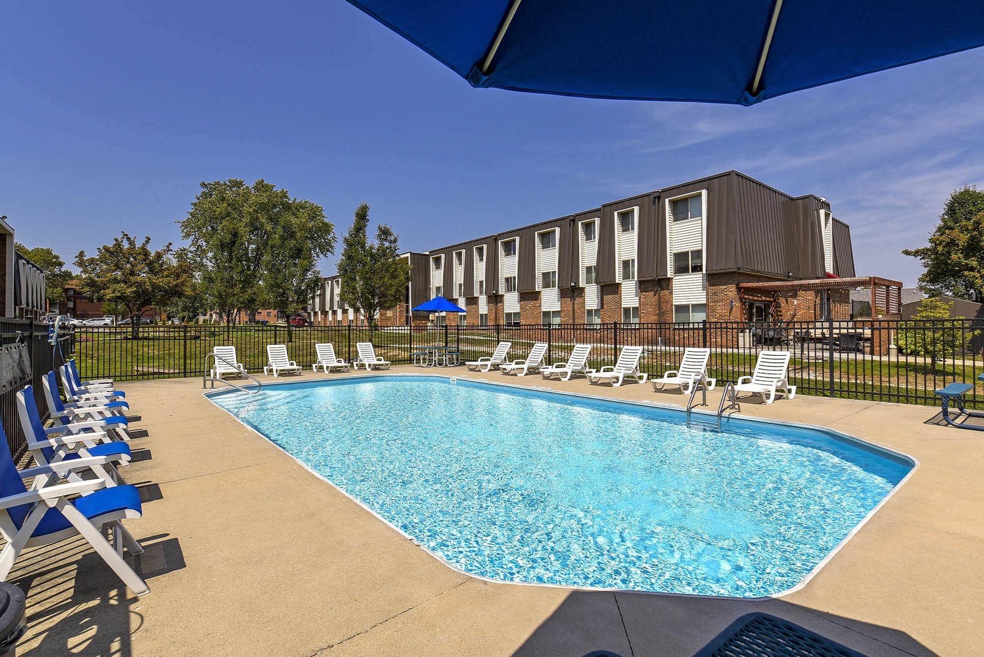 Outdoor community pool with white lounge chairs and blue umbrellas, surrounded by a fence at the Reserves at Arlington in Columbus, OH.