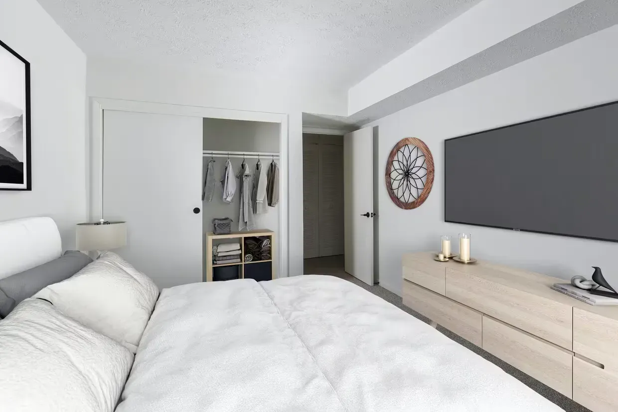 Modern apartment bedroom with a large bed, open closet, and low dresser under a wall-mounted TV at the Reserves at Arlington in Columbus, OH.