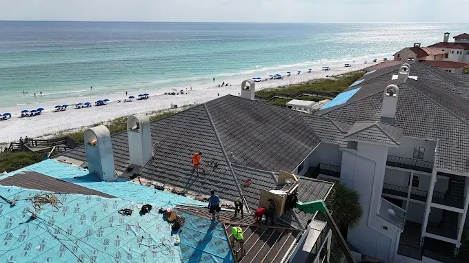 Roofers working on a building with a beach view; ocean, sand, and blue sky visible.