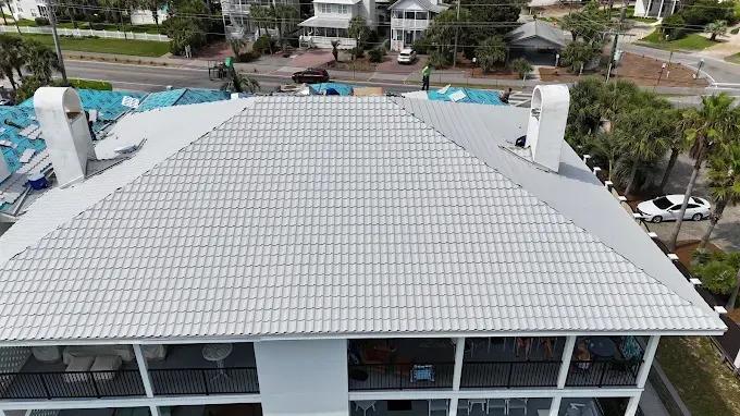 A white building with a tile roof, seen from above. Chimneys and trees are nearby.