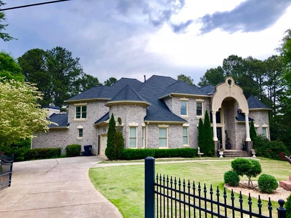 Two-story brick home with dark roof, arched entryway, and wrought iron fence on a cloudy day.