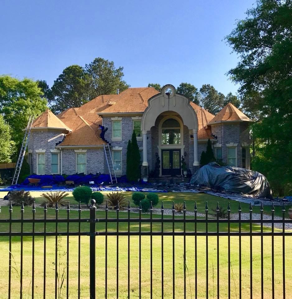 Large brick house with new brown roof; workers on ladders.