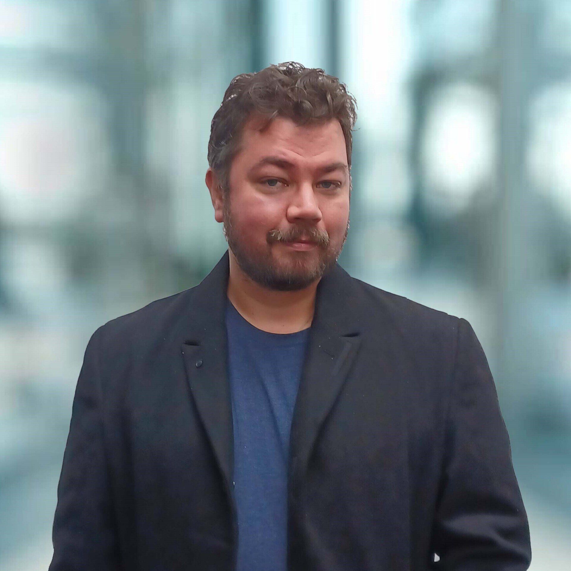 A man with a beard wearing a black jacket and a blue shirt
