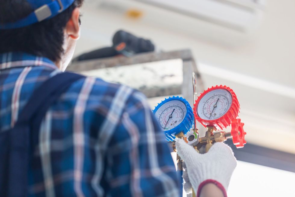 Technician in blue plaid shirt uses manifold gauges on HVAC equipment indoors