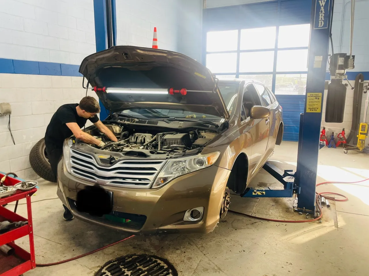 Mechanic works on a brown car with its hood open inside a garage. | Equality Automotive