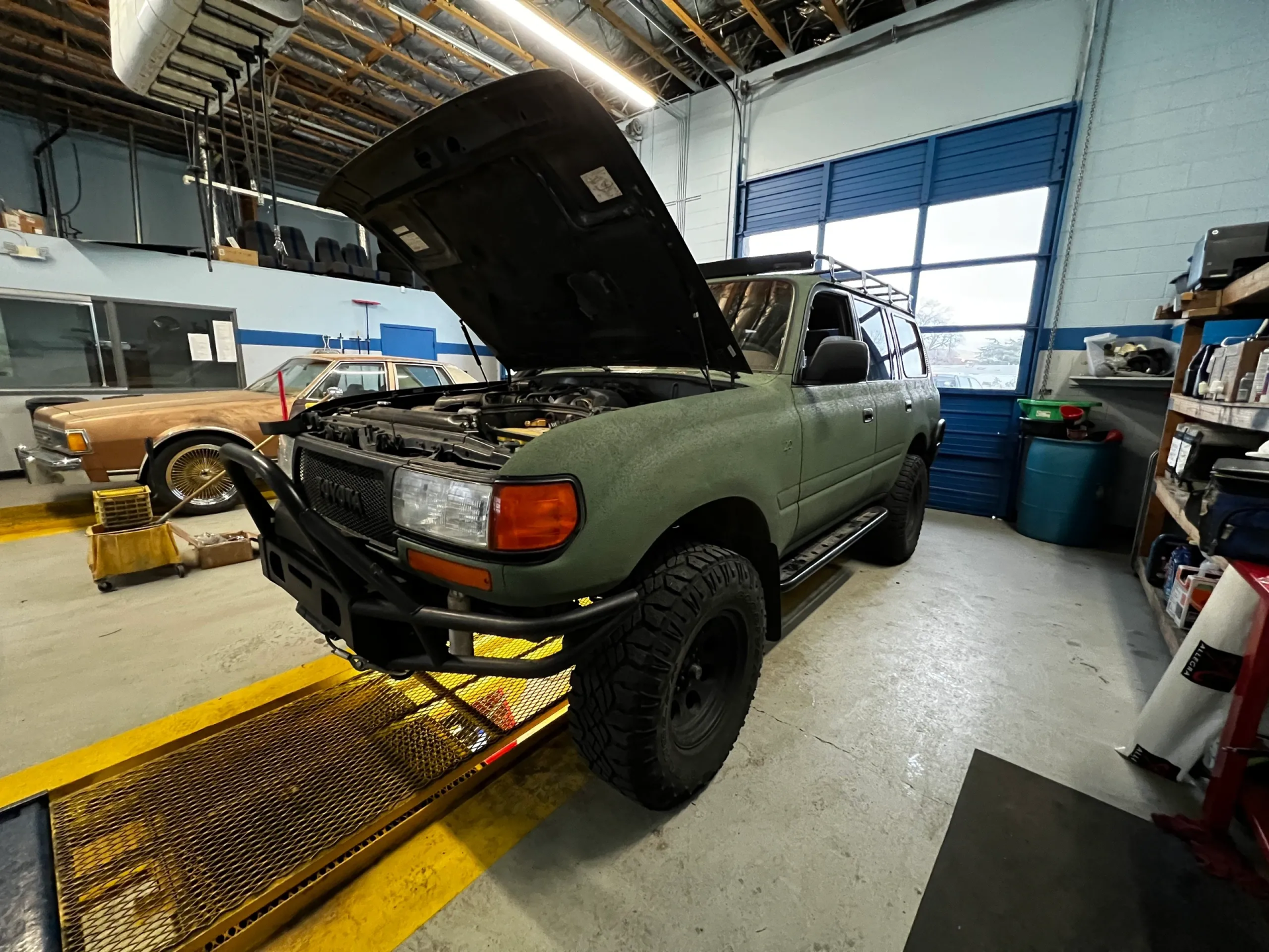 Green Toyota Land Cruiser with hood open in a garage, parked on a lift. | Equality Automotive