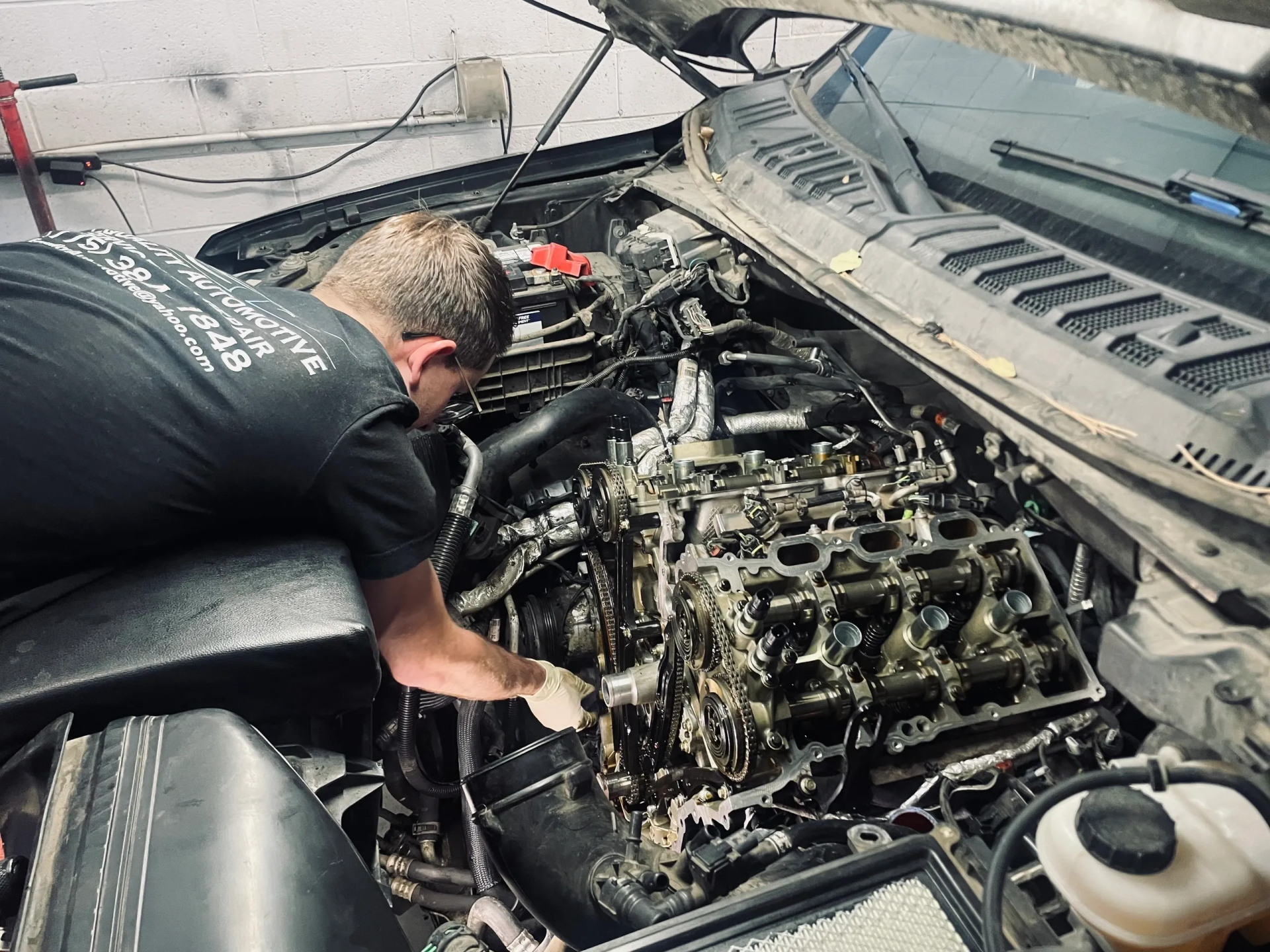 Mechanic working on a car engine, covered in oil, in a garage setting. | Equality Automotive