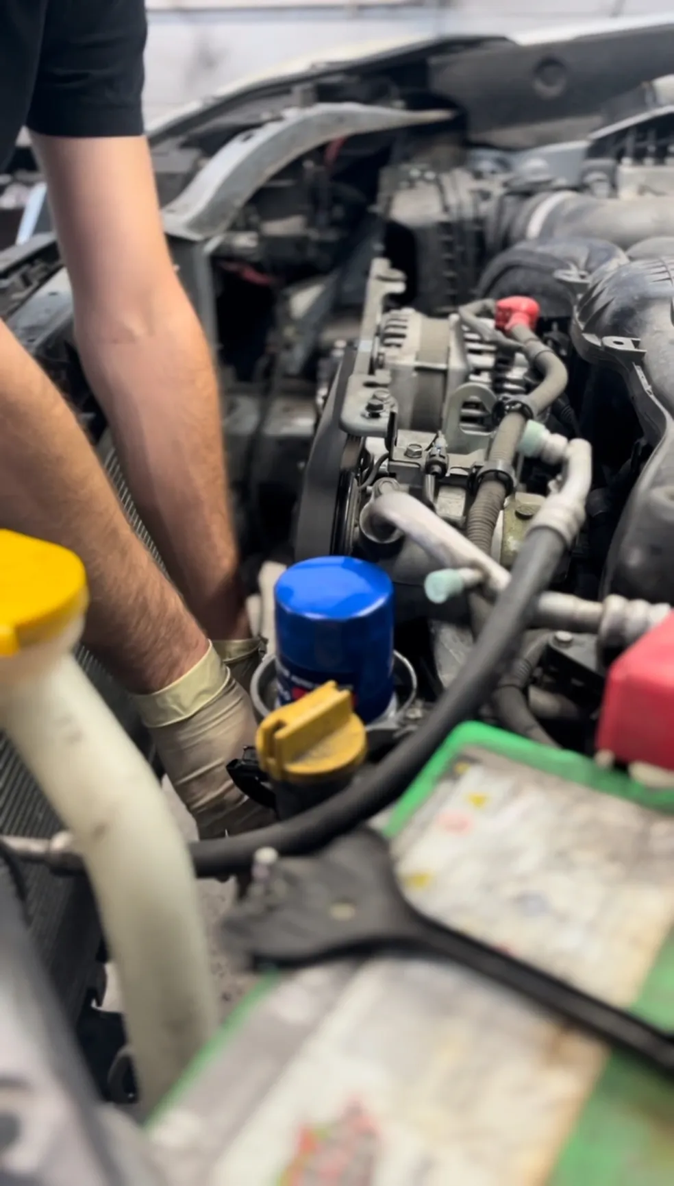 Mechanic working on a car engine; hands in engine bay near a blue oil filter. | Equality Automotive