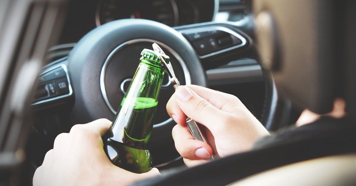 A person is holding a bottle of beer in their hand while driving a car.
