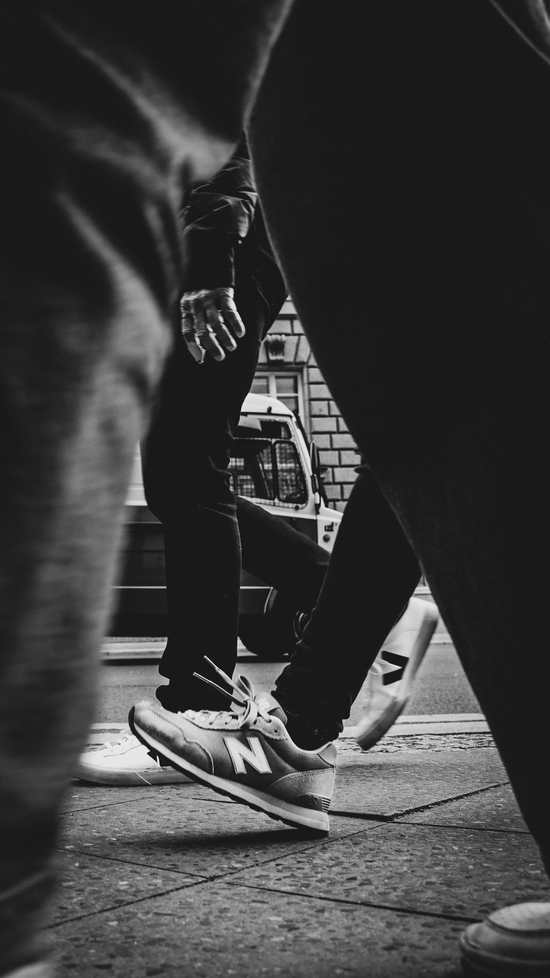 People walking down a street; one person's shoes are in focus. Black and white.