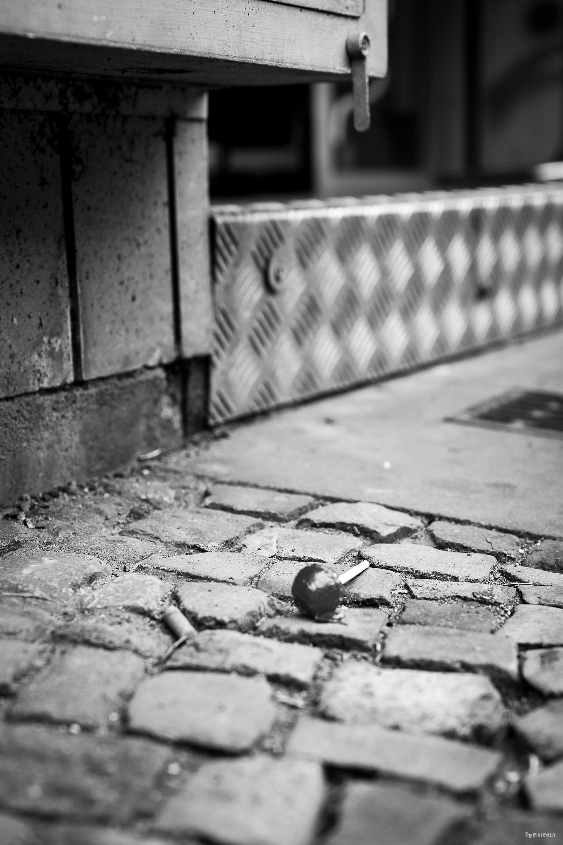Cigarette butt on brick pavers next to a building with a metal diamond plate panel.