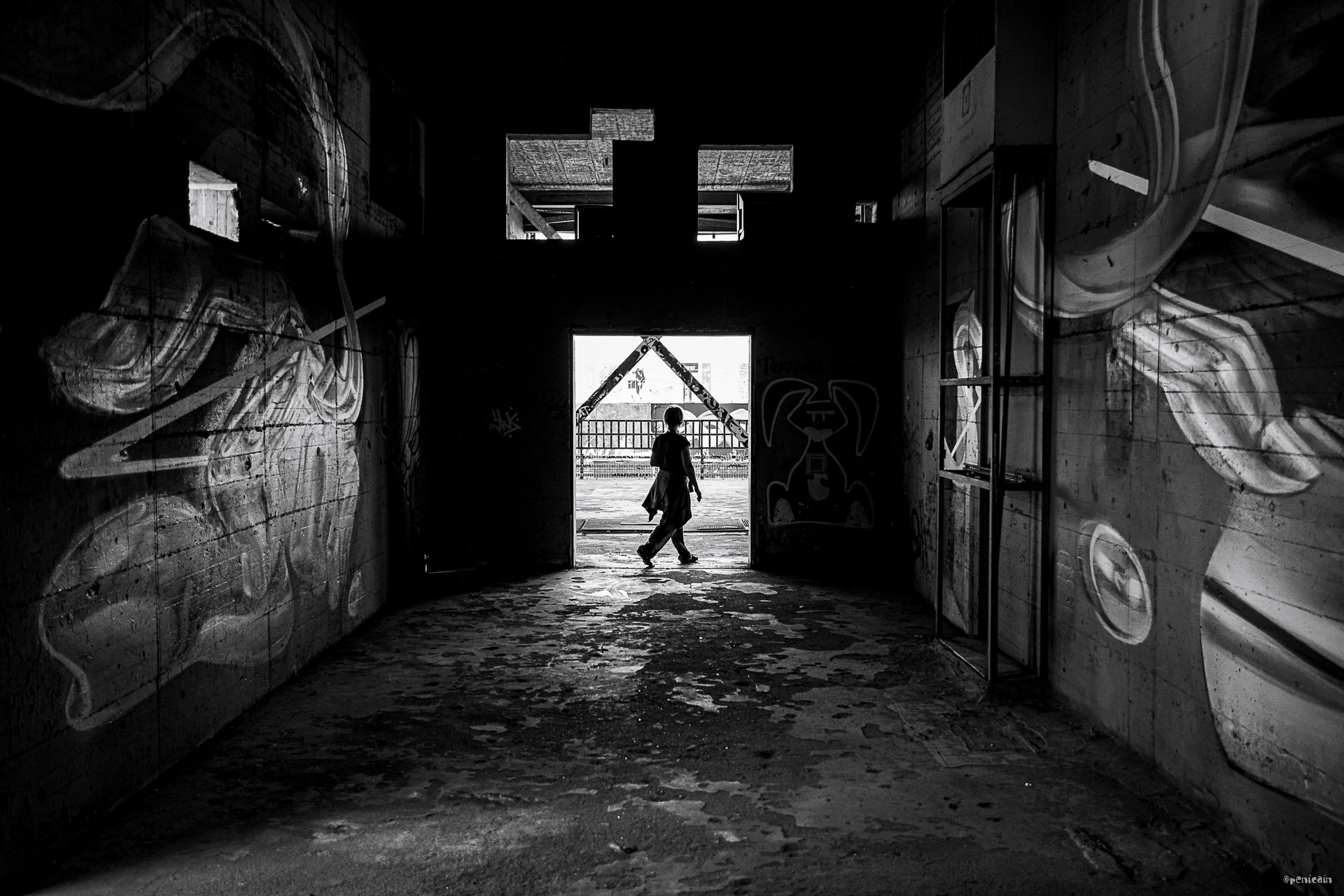 Dark, graffiti-covered hallway with a figure walking towards the bright doorway at the end.