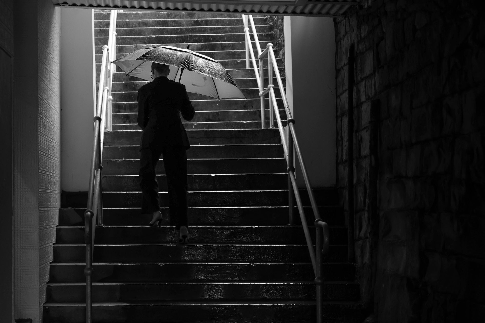Man with umbrella climbs stairs in rain. Black and white.