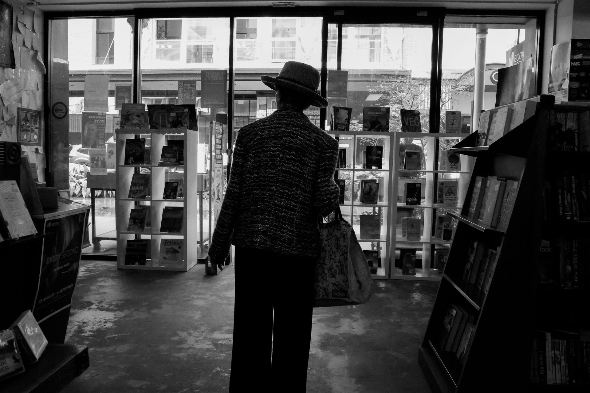 Person in hat, inside a bookstore, browsing shelves. Black and white.