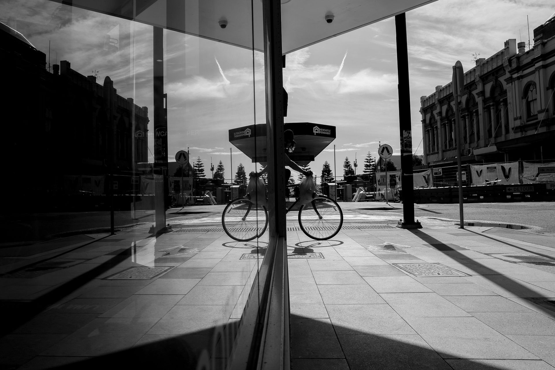 Black and white photo: Bicycle reflected in a glass building's window on a city street.