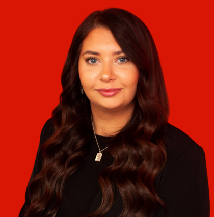 Woman with long, wavy brown hair, wearing a black shirt and silver necklace, against a red background.