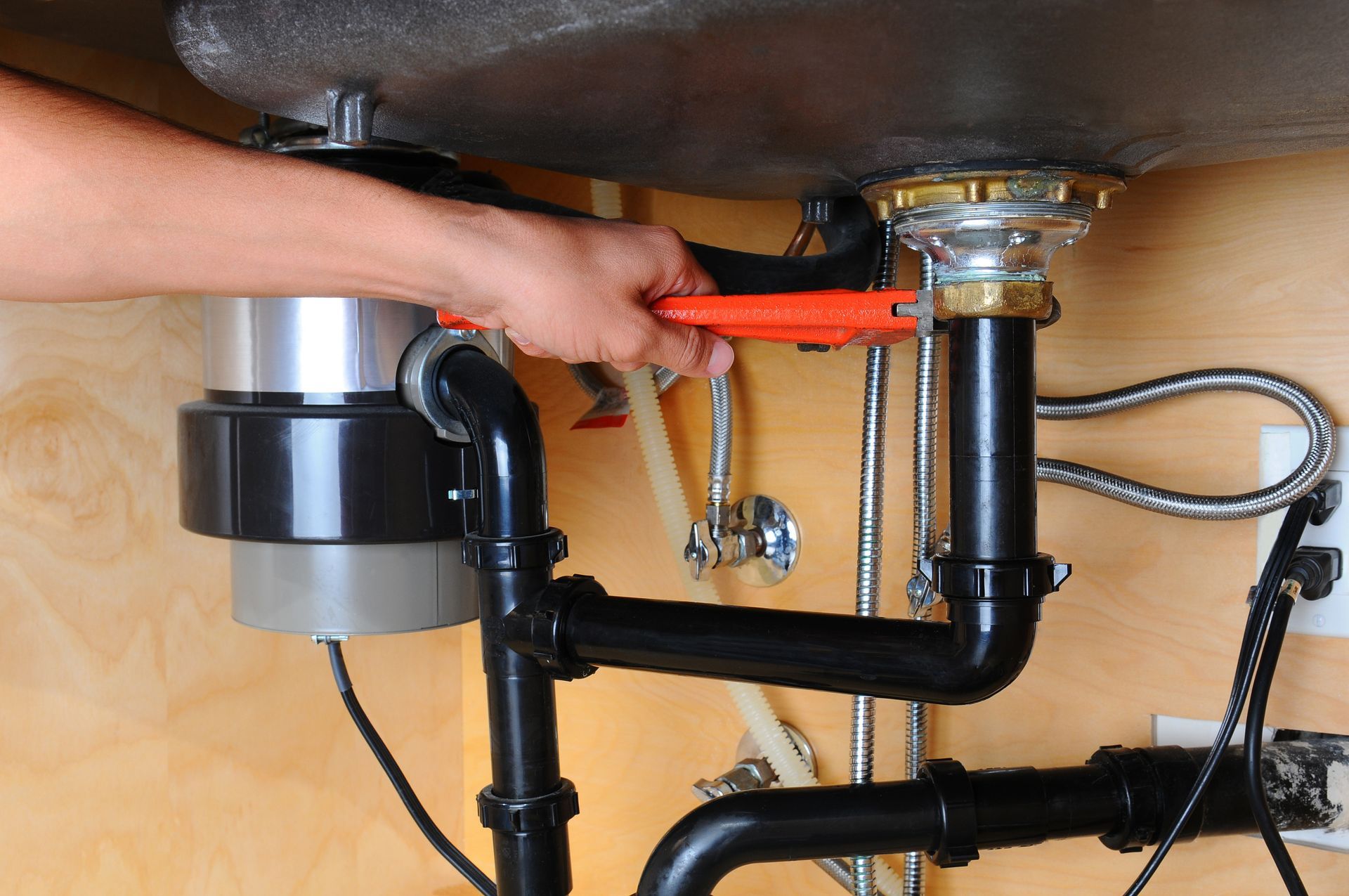 Plumber fixing pipes under a kitchen sink with a wrench.