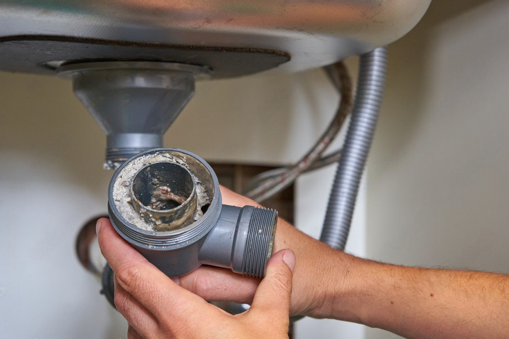 Hand of plumber holding joints and connections of sink in a bathroom.