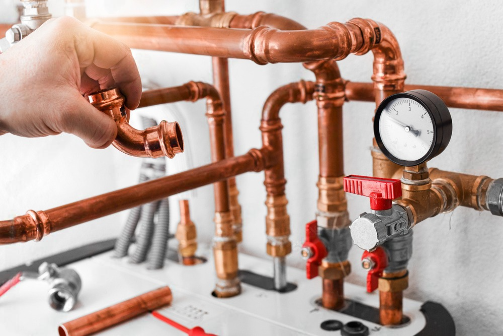 a man is working on copper pipes with a red valve