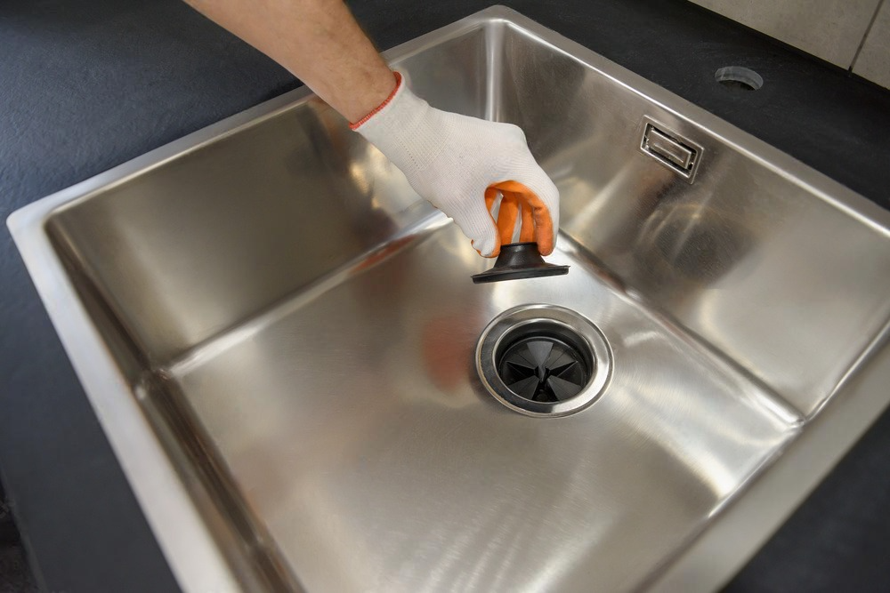 Hand gripping kitchen waste shredder lid, ready for use.