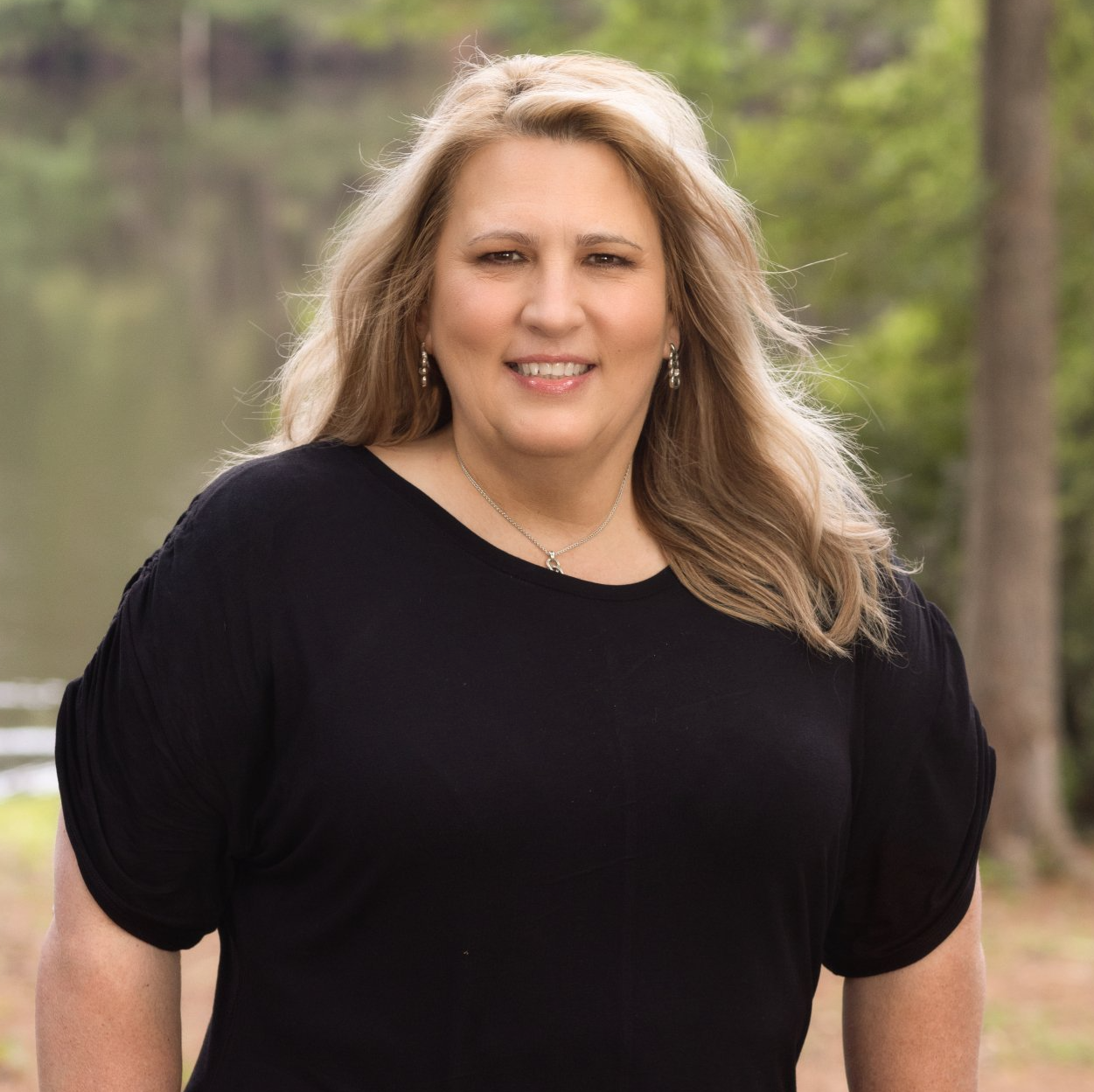 A woman in a black shirt is standing in front of a lake.