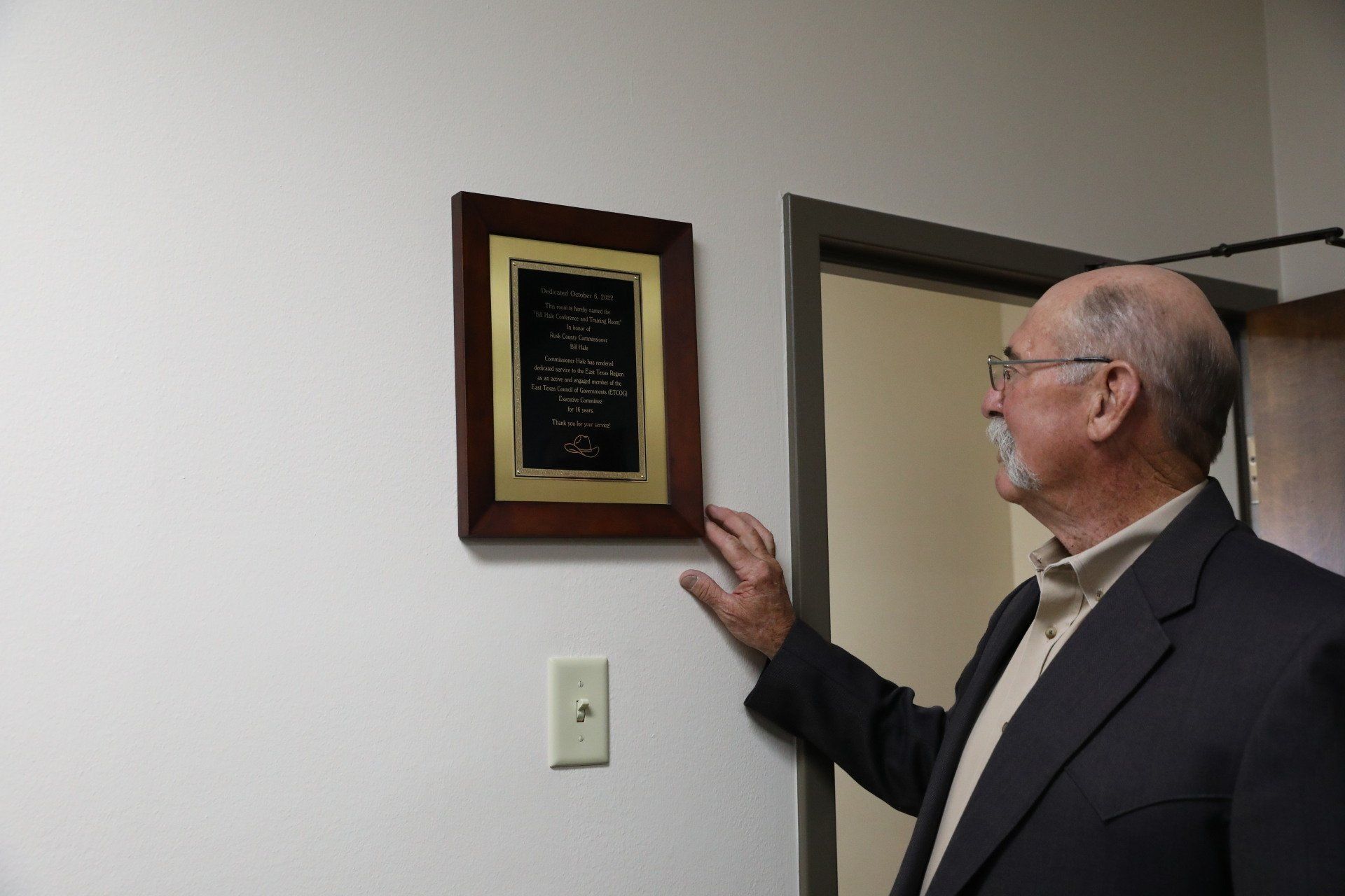 A man in a suit is pointing at a framed picture on a wall.