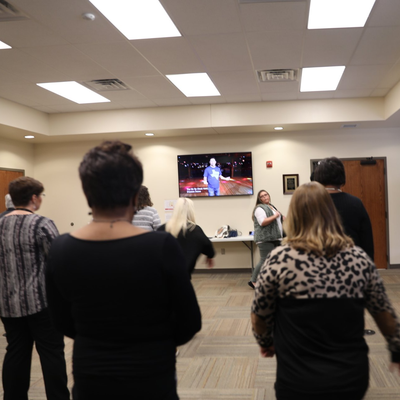 A group of people are standing in a room watching a tv