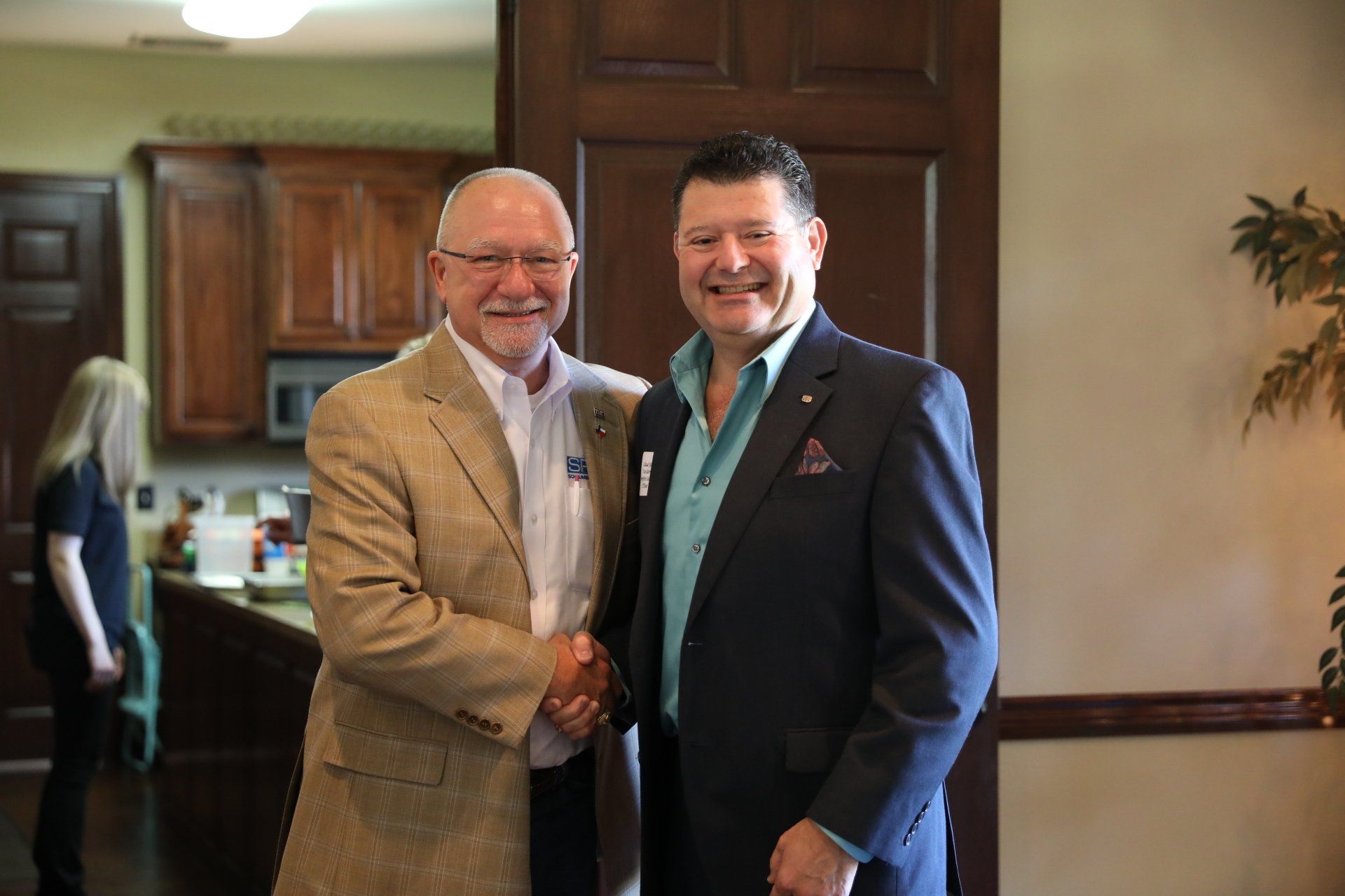 Two men in suits are shaking hands in a room.