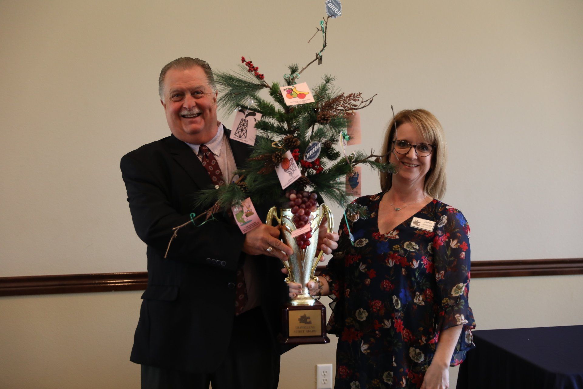 A man and a woman are holding a trophy in front of a christmas tree.