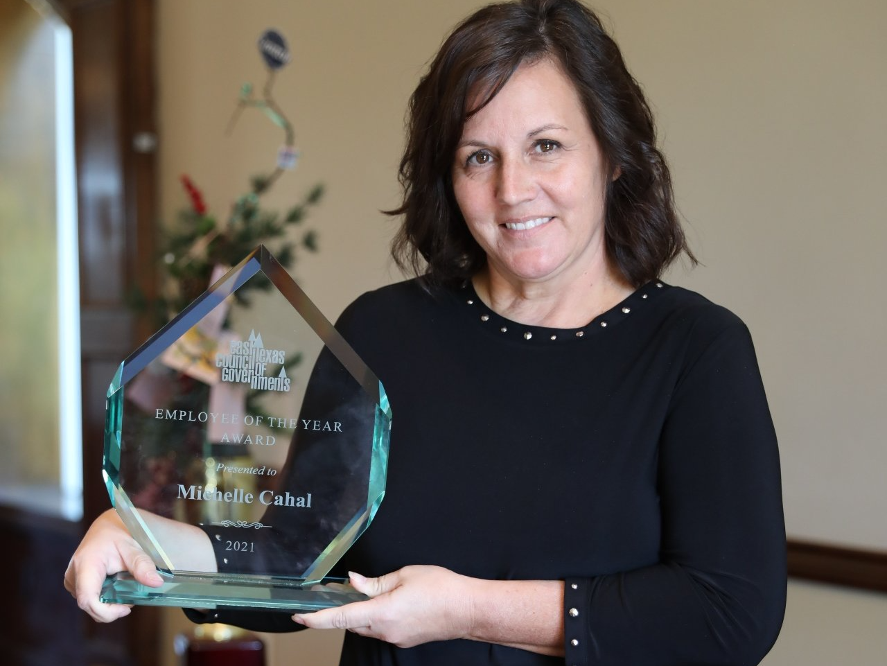 A woman in a black shirt is holding a glass award