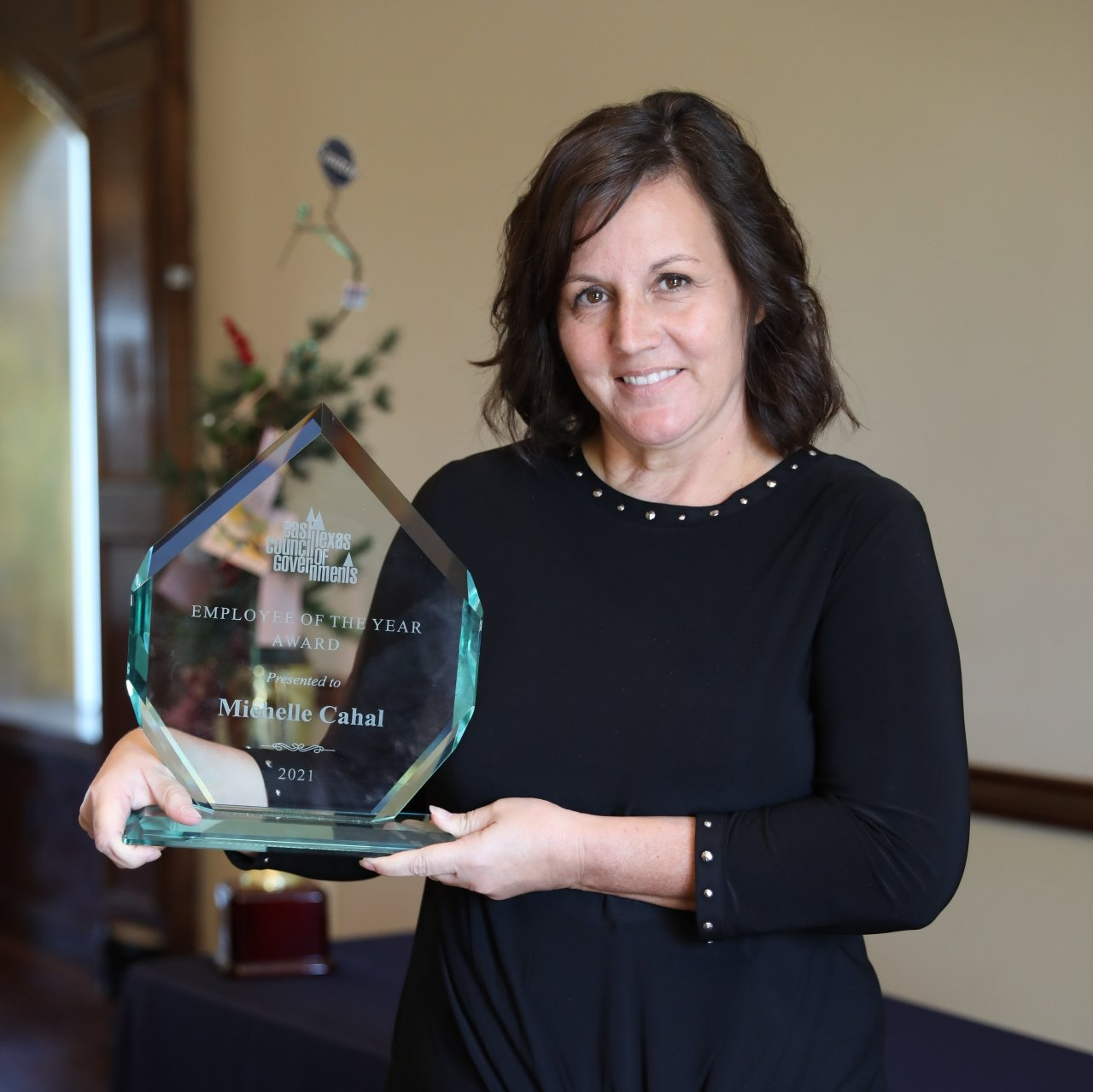 A woman in a black dress is holding a glass award