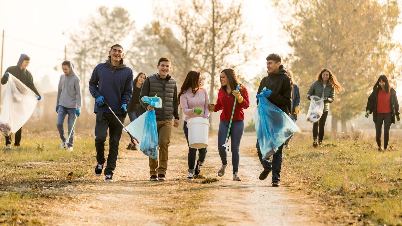 A group of people are walking down a dirt road holding trash bags.