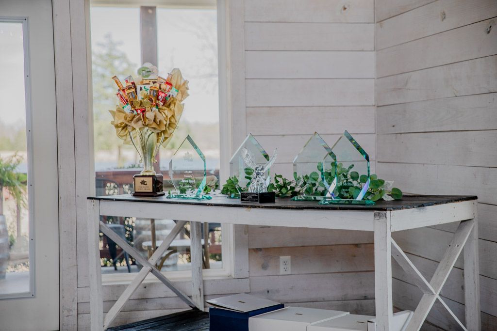 White table with awards and flowers, against a white shiplap wall by a window.