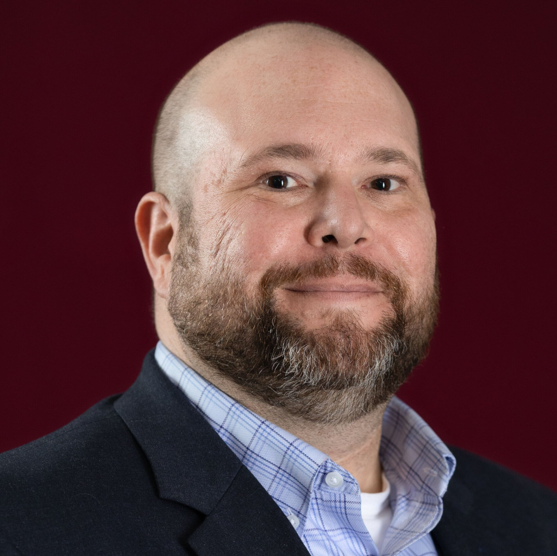 A bald man with a beard is wearing a suit and smiling.