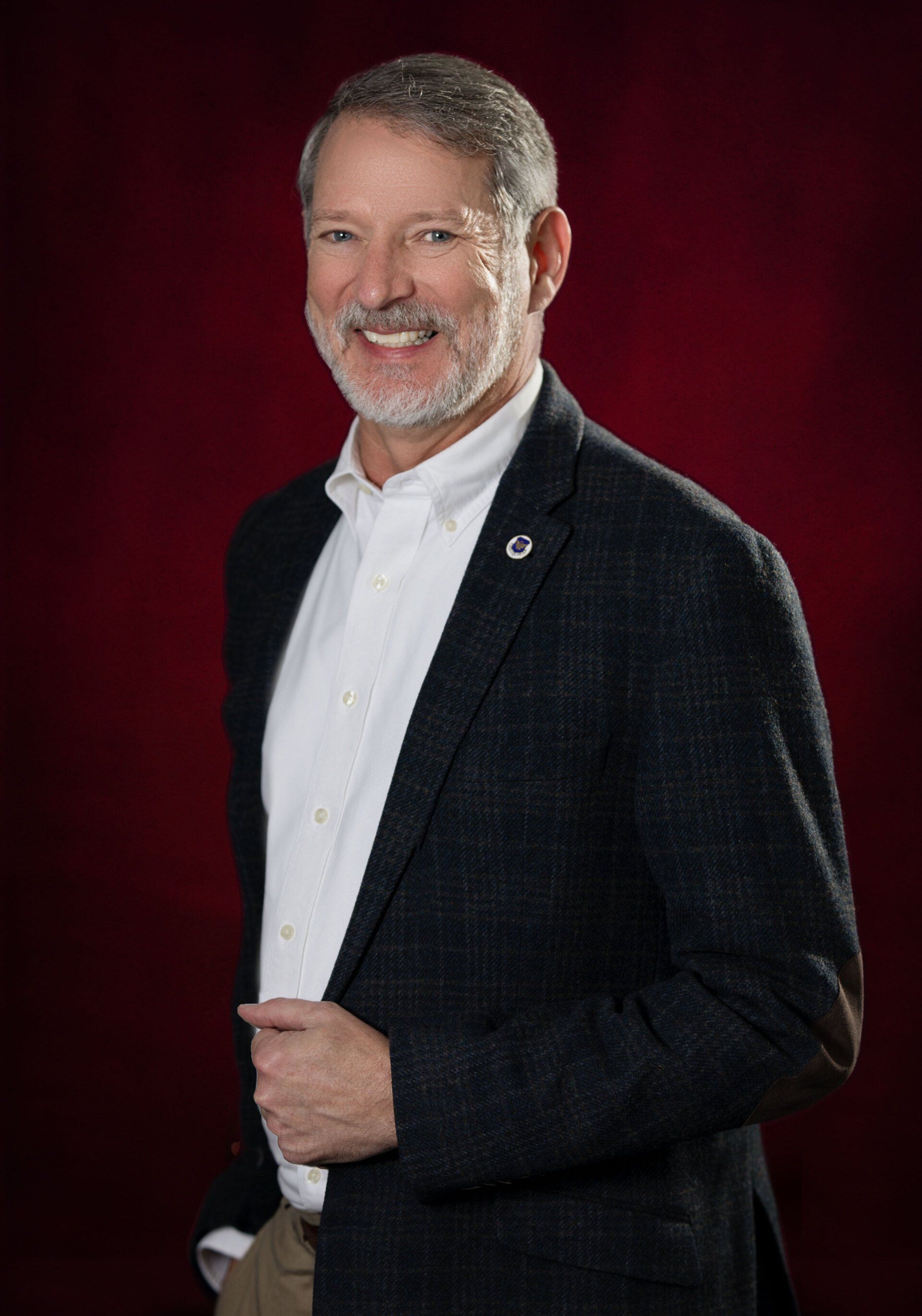 A man in a suit and white shirt is standing in front of a red background.
