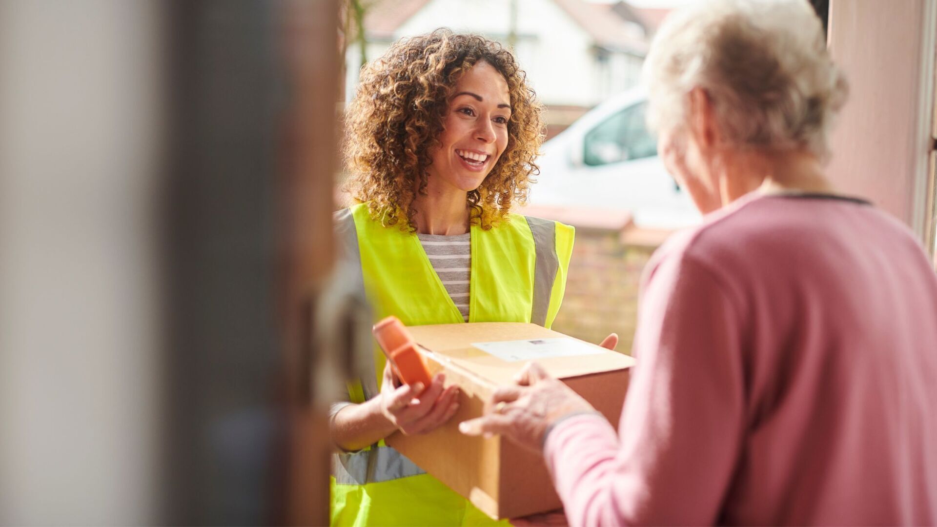 A woman in a yellow vest is delivering a box to an elderly woman.