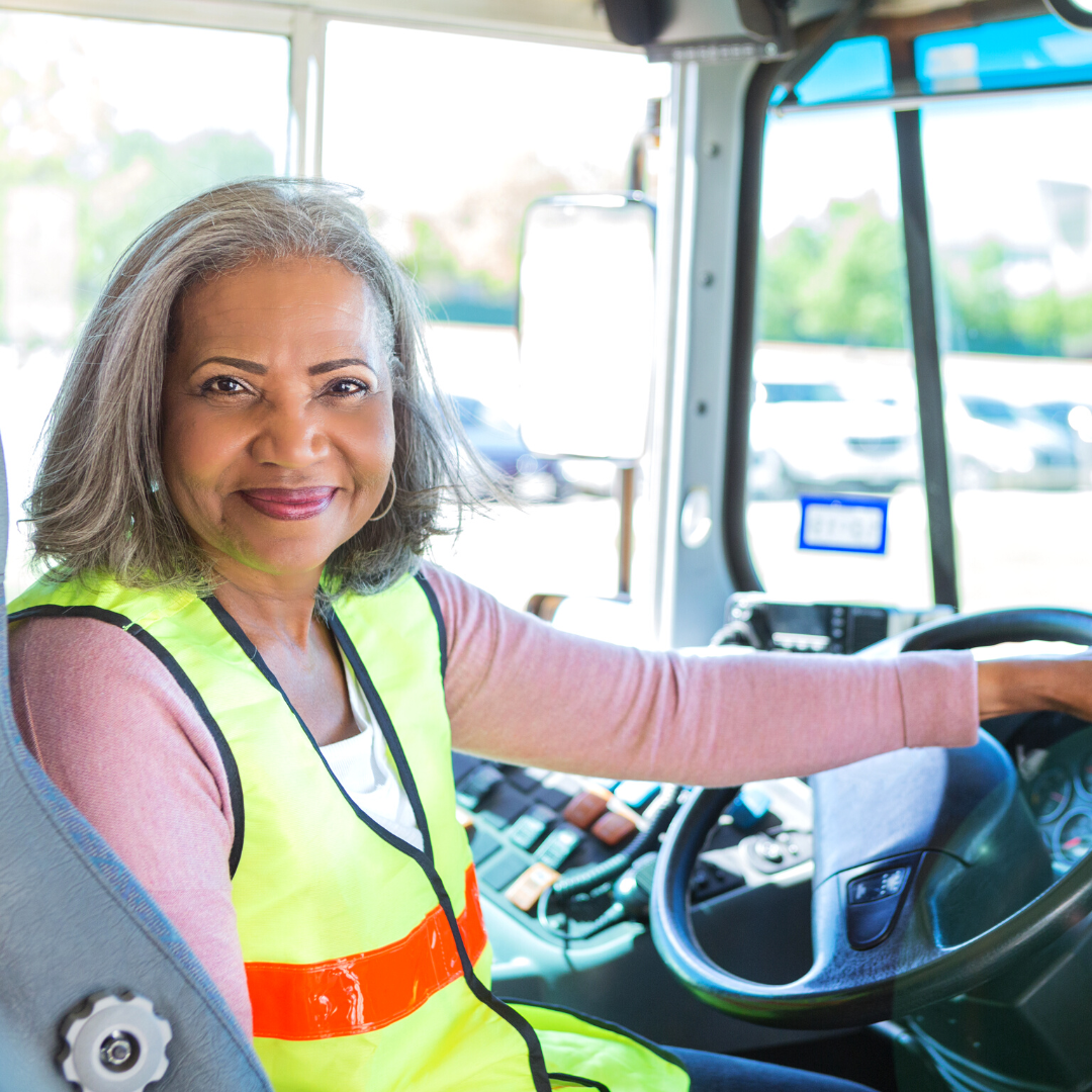 A woman in a yellow vest is sitting in the driver 's seat of a bus