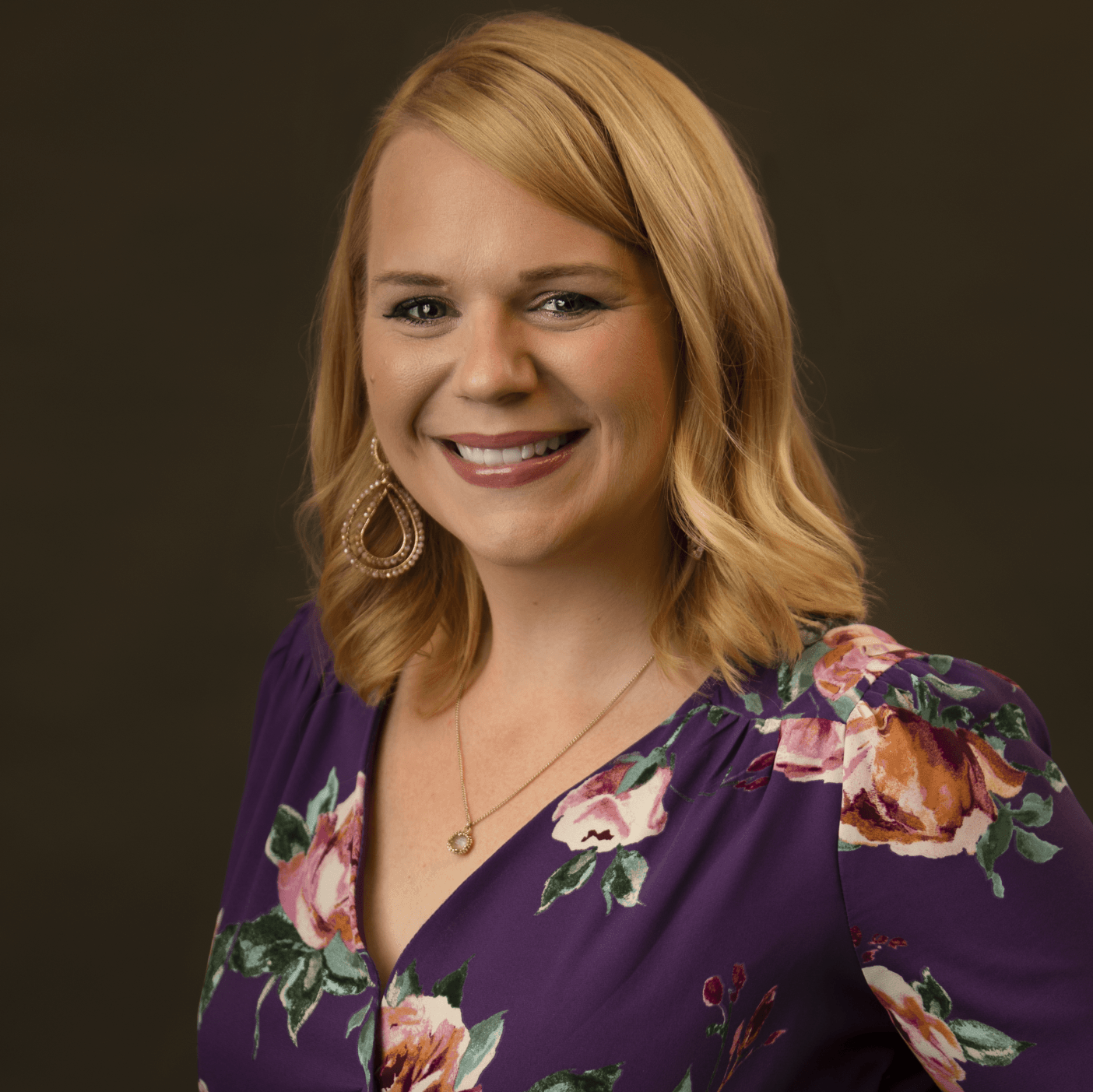 A woman in a purple floral dress is smiling for the camera.